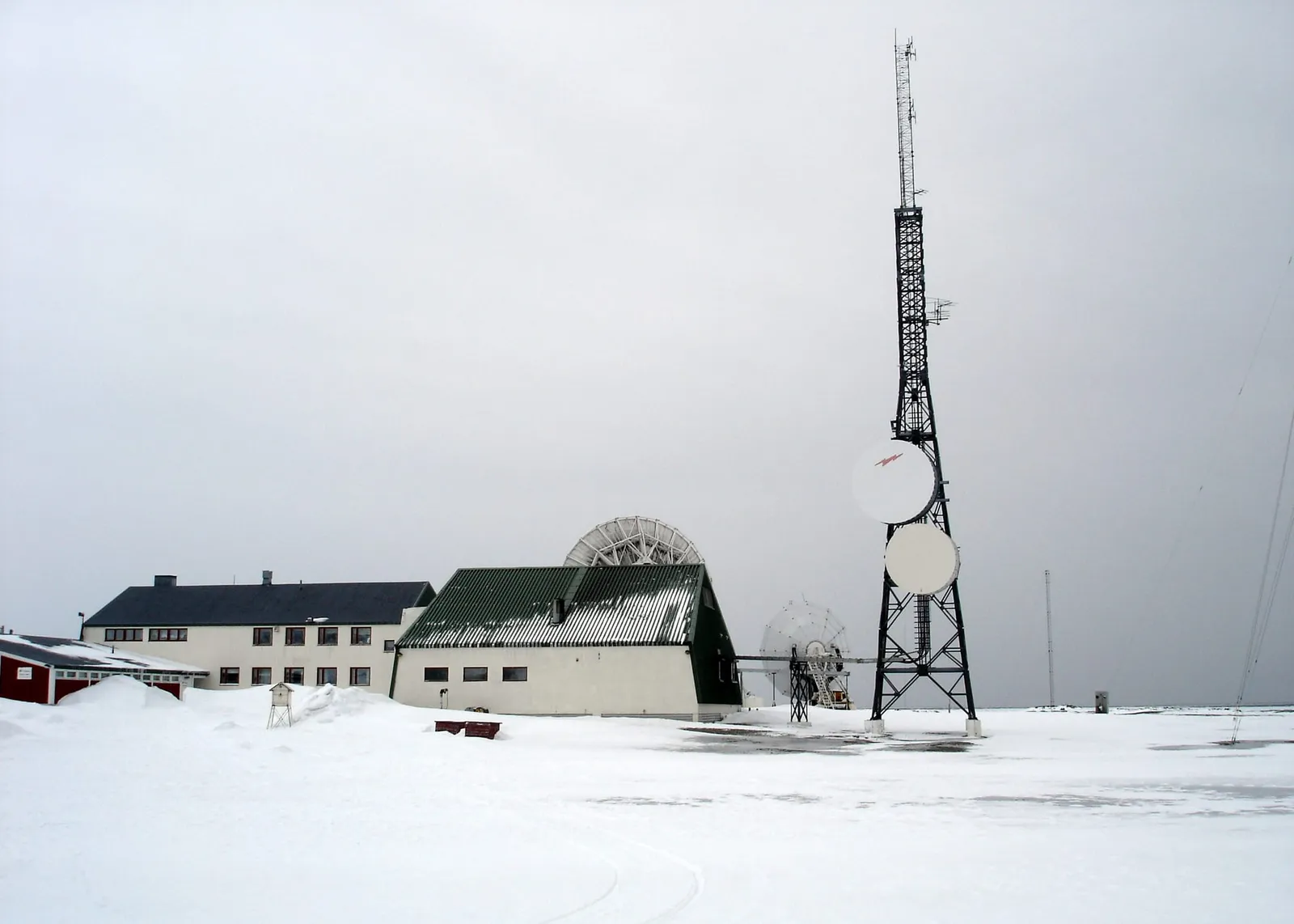 The white buildings of Isfjord Radio in the snow, with a tall lattice radio mast and satellite dishes beside them