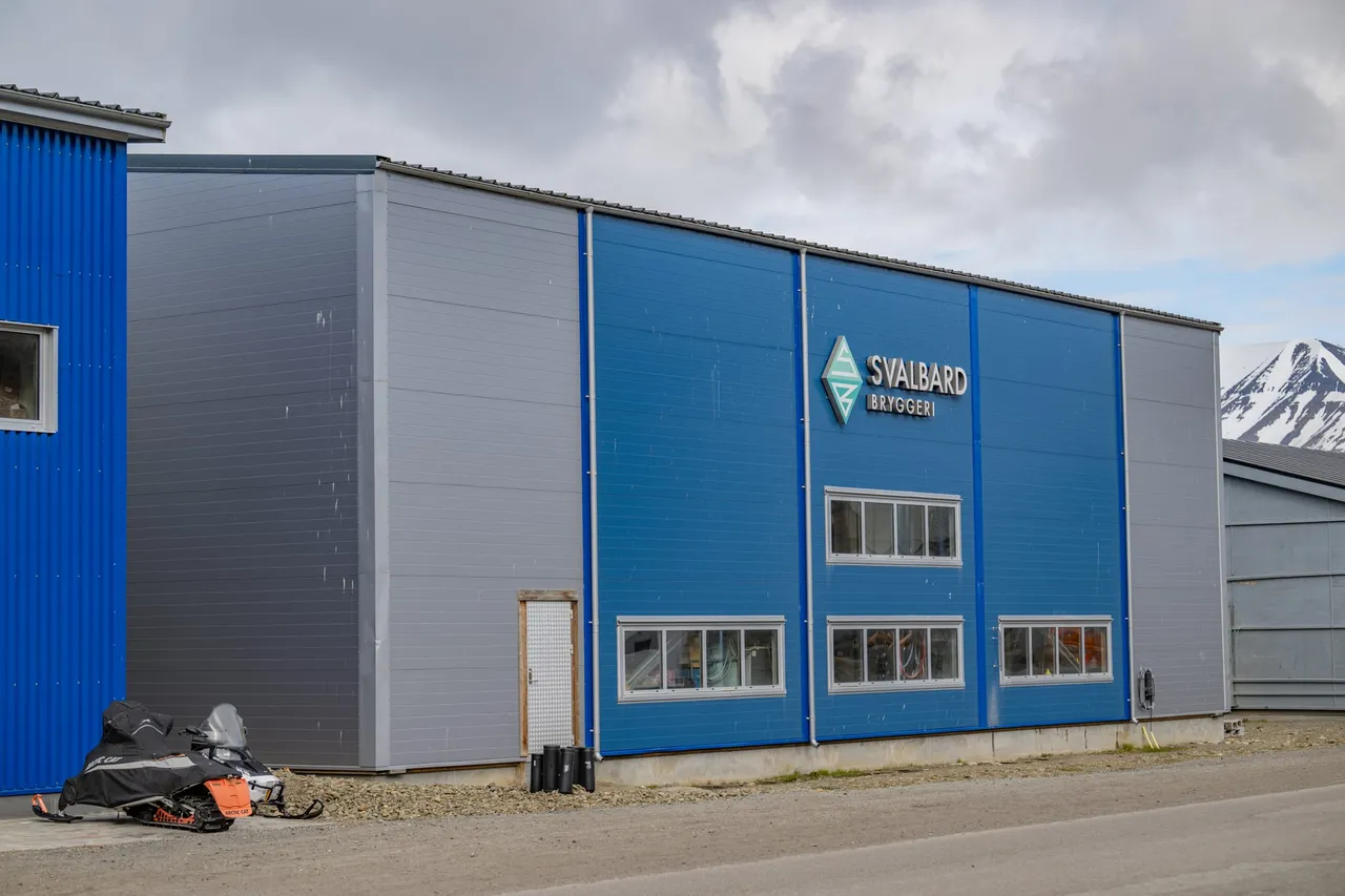 The blue and grey building of Svalbard Brewery, with its logo on the wall and a snowmobile parked outside