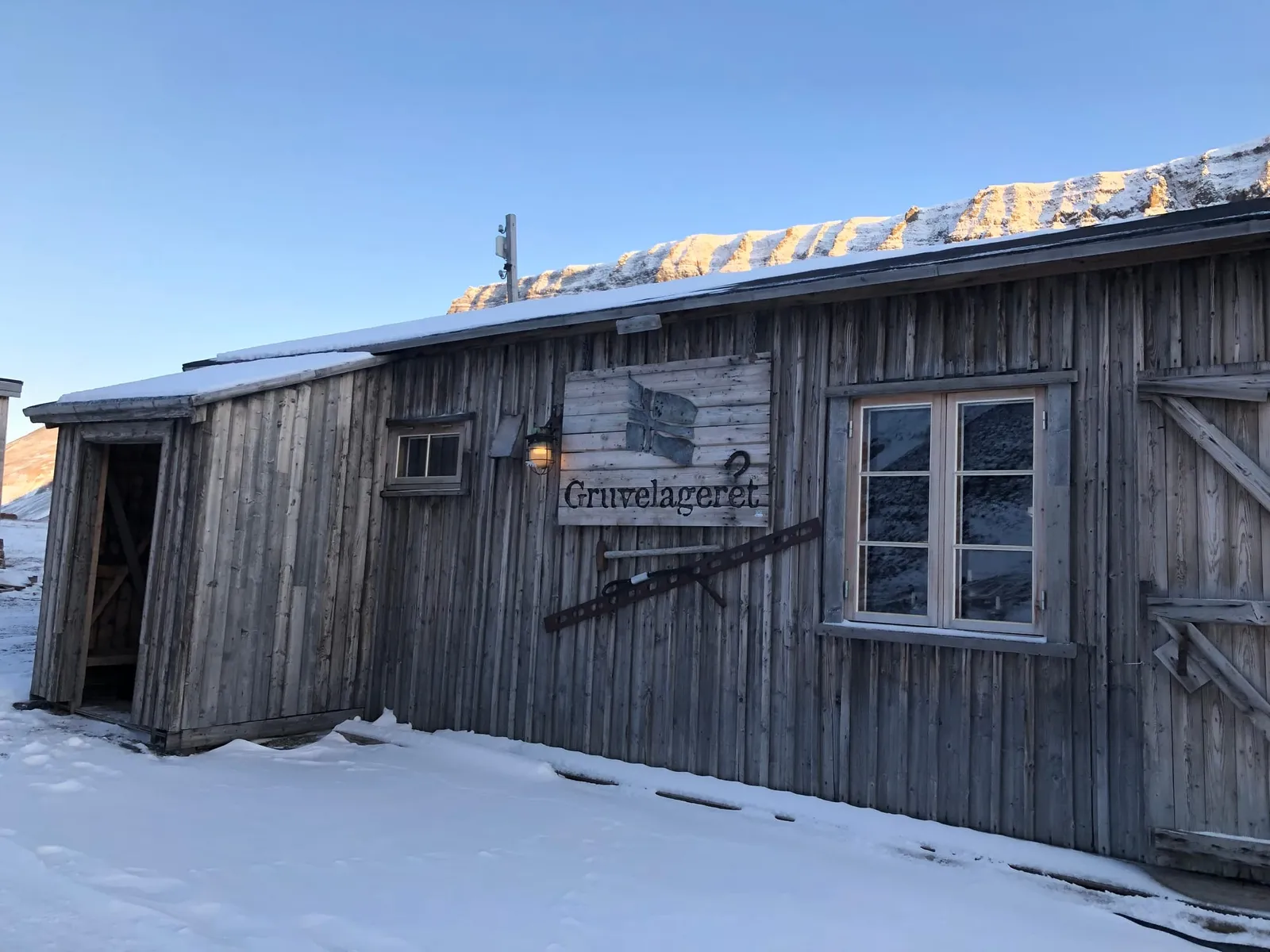 The weathered timber walls of Gruvelageret, an old mining warehouse turned restaurant, with its sign above the door and snowy mountains behind