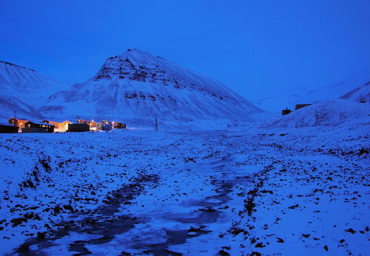 Houses in Nybyen lit up below a snow-covered mountain, everything washed in deep blue light